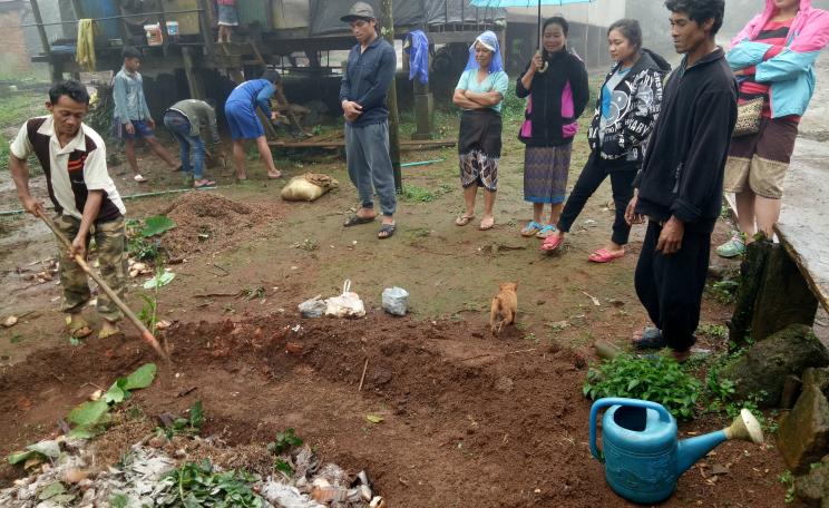Chon hoes compost for his coffee crop as his family look on.